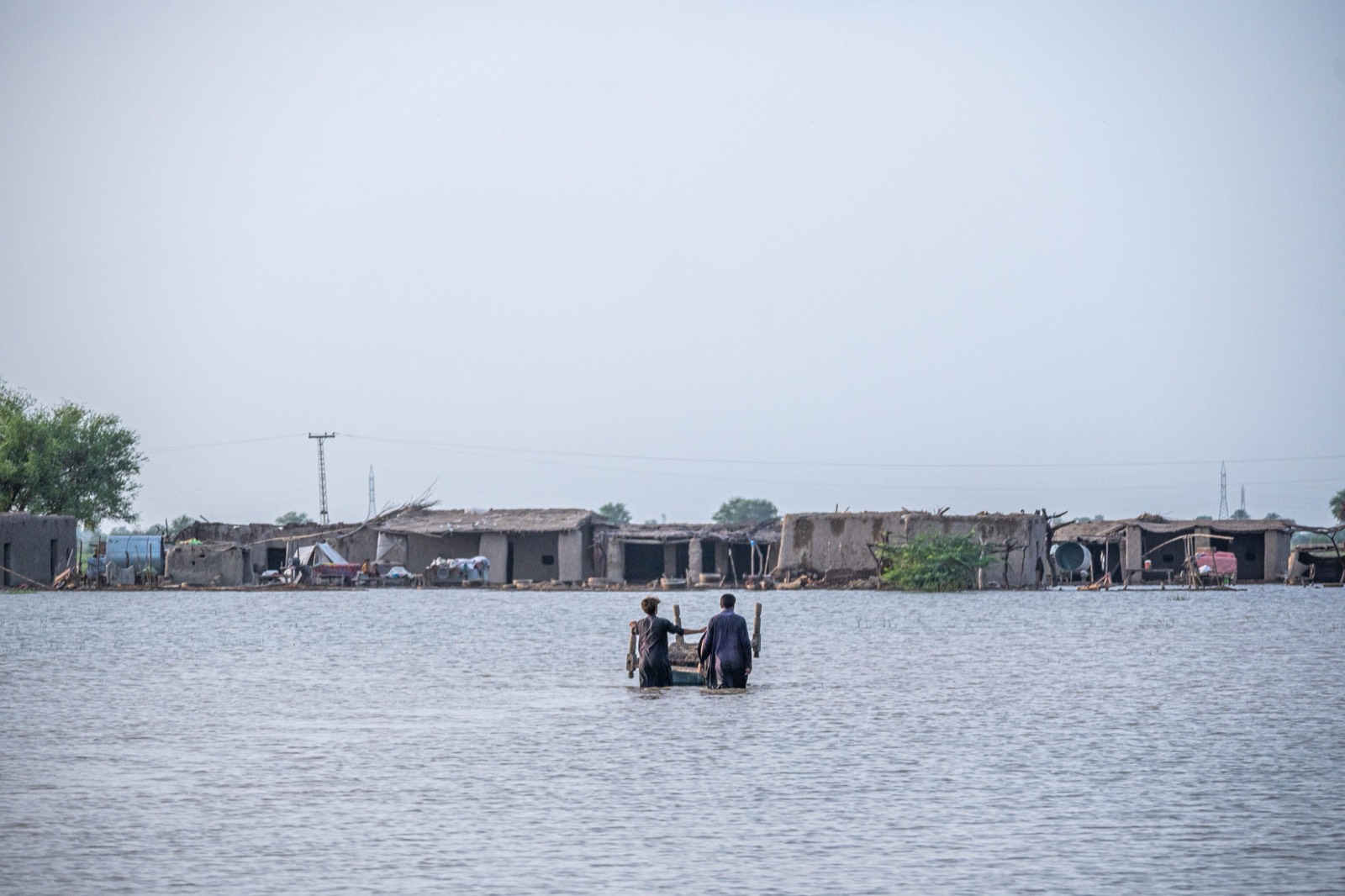 Residents wading through deep floodwater toward homes submerged nearly to the rooftops