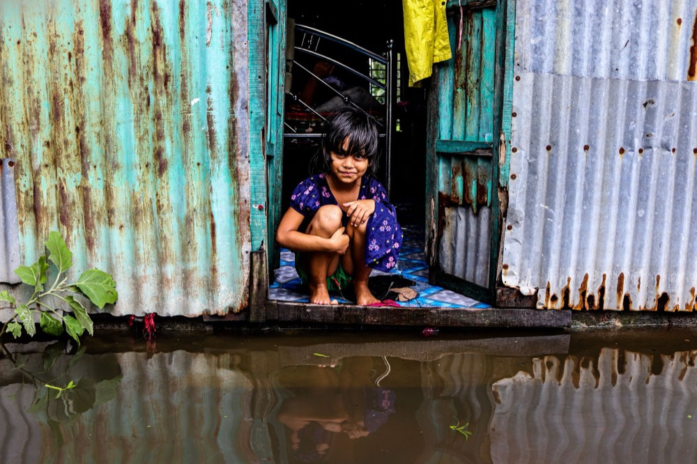 A young girl crouches in the doorway of her home as floodwater reaches the threshold